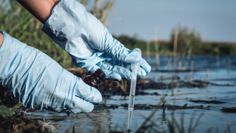 Un scientifique en train de prélever l'eau d'une rivière pour l'analyser